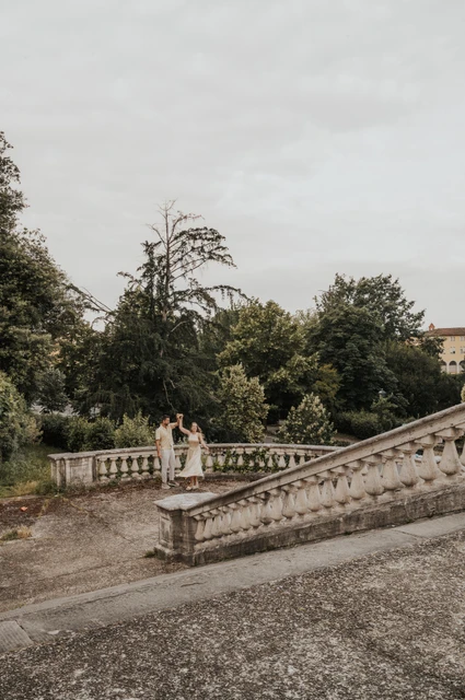 A wider stairway view during a Florence proposal photoshoot The couple stand together beyond a stone stairway balustrade, surrounded by greenery, during their Florence proposal photoshoot.