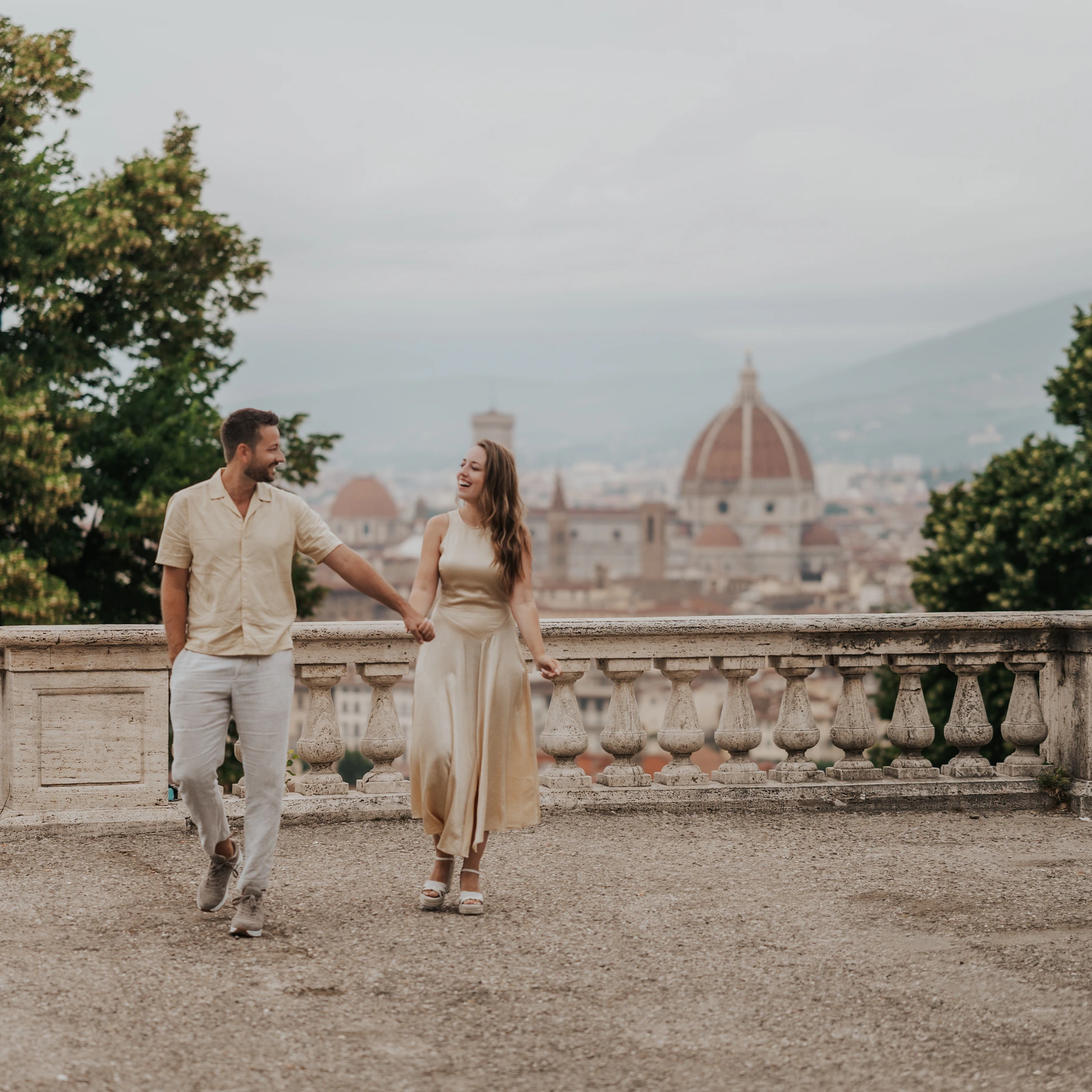 Una coppia si tiene per mano accanto a una balaustra in pietra sopra Firenze, con la cupola del Duomo sullo sfondo.