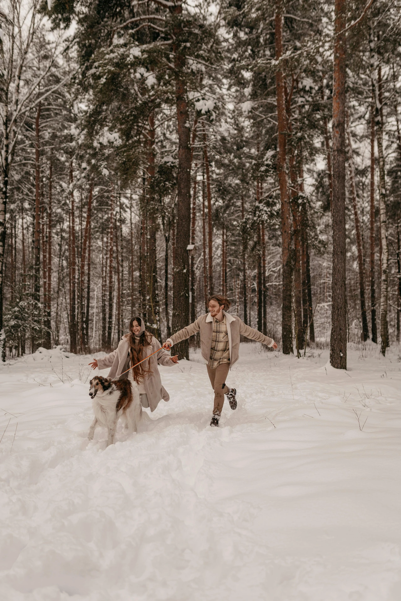 Couple and dog running through snowy forest in coordinated outfits