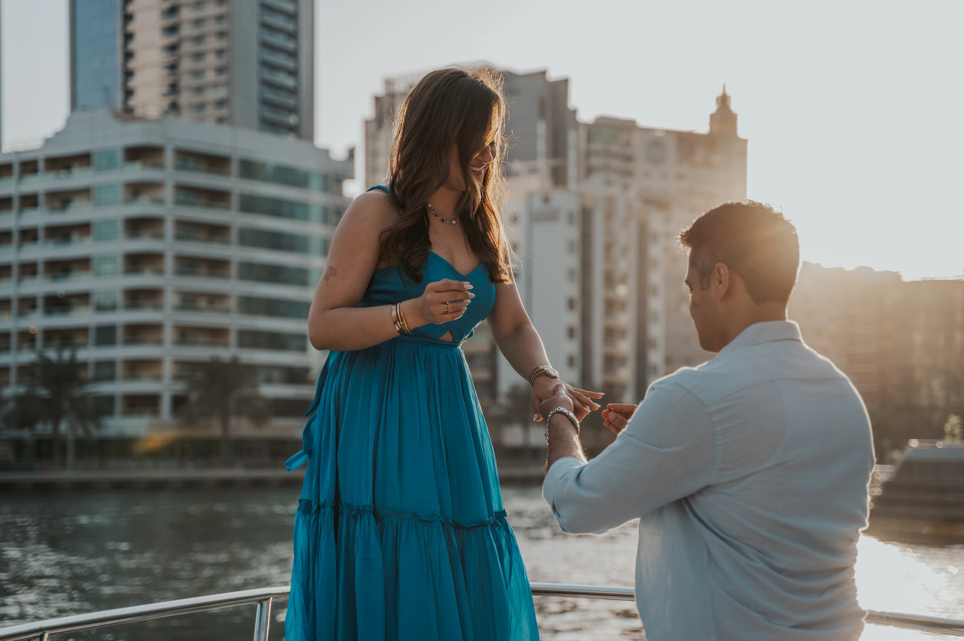 Prosi o rękę na łodzi w Dubaju Mężczyzna klęczy przed partnerką i trzyma jej dłoń podczas oświadczyn na łodzi, z panoramą Dubaju w tle.