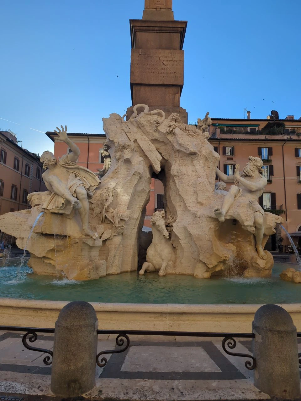 Pantheon and Piazza Navona Photoshoot - Four Rivers Fountain The Fountain of the Four Rivers fills Piazza Navona with sculpted figures, flowing water and a tall obelisk beneath blue sky.