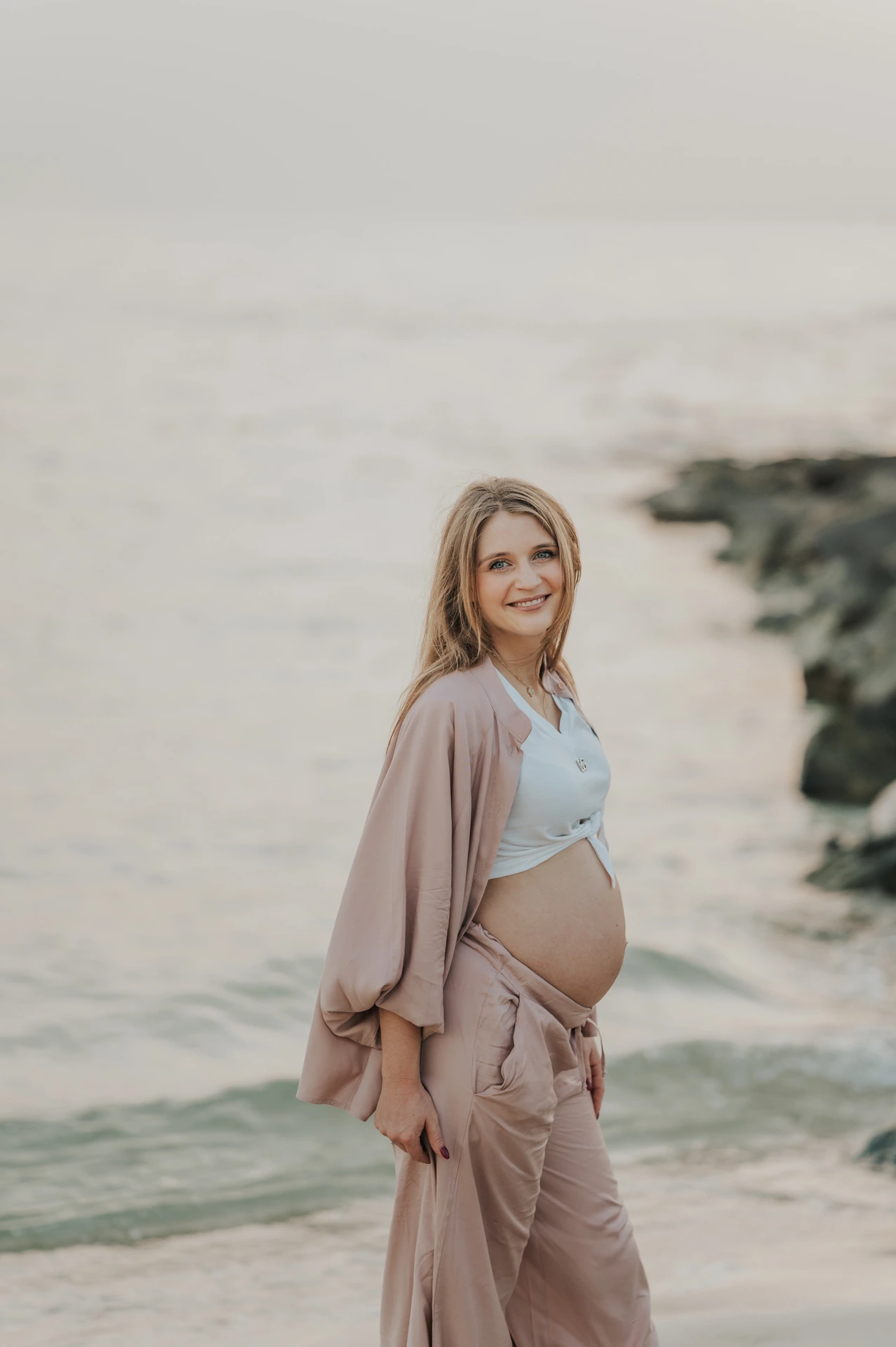 A pregnant woman stands near the shoreline in Dubai during a gentle beach maternity portrait for a gender reveal photoshoot.