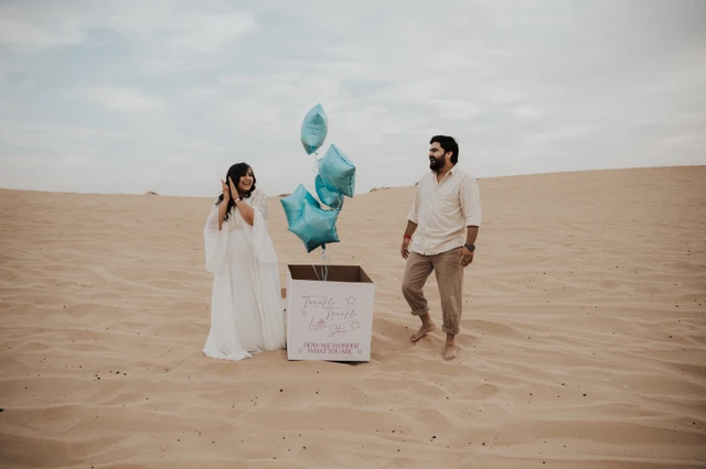 A couple stands beside a reveal box with blue star balloons on Dubai desert dunes during a styled gender reveal photoshoot.
