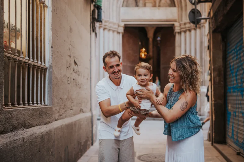 60-minutenfotoshoot Barcelona - Straat in de Gotische Wijk Twee volwassenen tillen een lachende peuter tussen hen in een smal straatje in de oude stad van Barcelona tijdens een fotoshoot van 60 minuten in Barcelona.