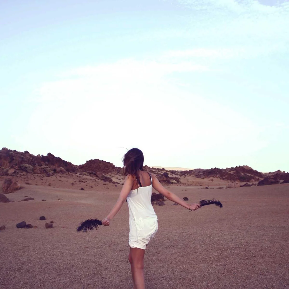 Woman in white dress with arms outstretched in desert landscape at sunset