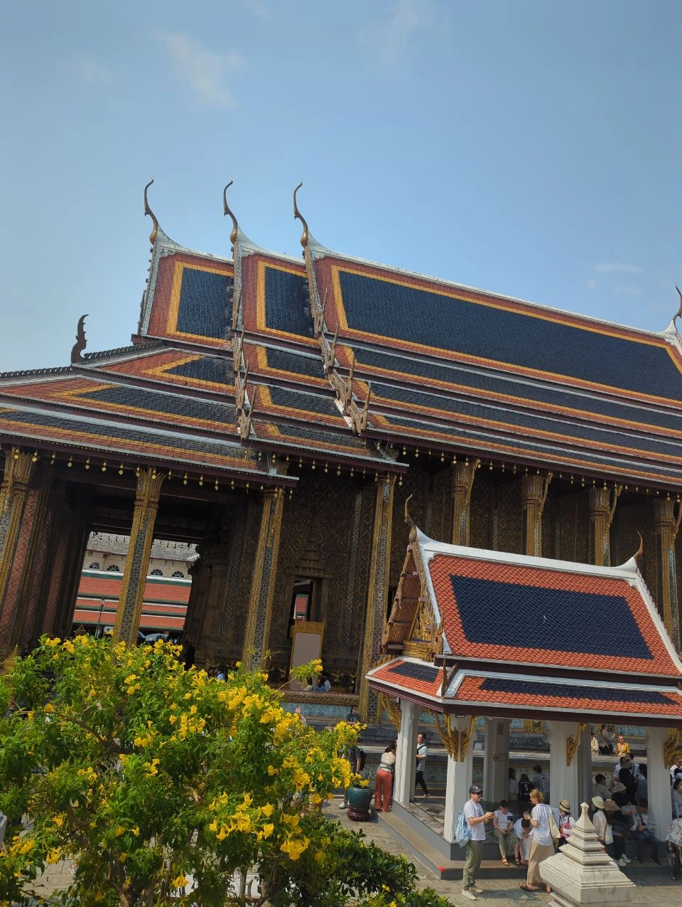 Bangkok Temple Outfit: Grand Palace Details Visitors walk beneath richly decorated roofs and gold-trimmed columns in Bangkok’s Grand Palace, showing the detailed backdrop of a temple photoshoot.