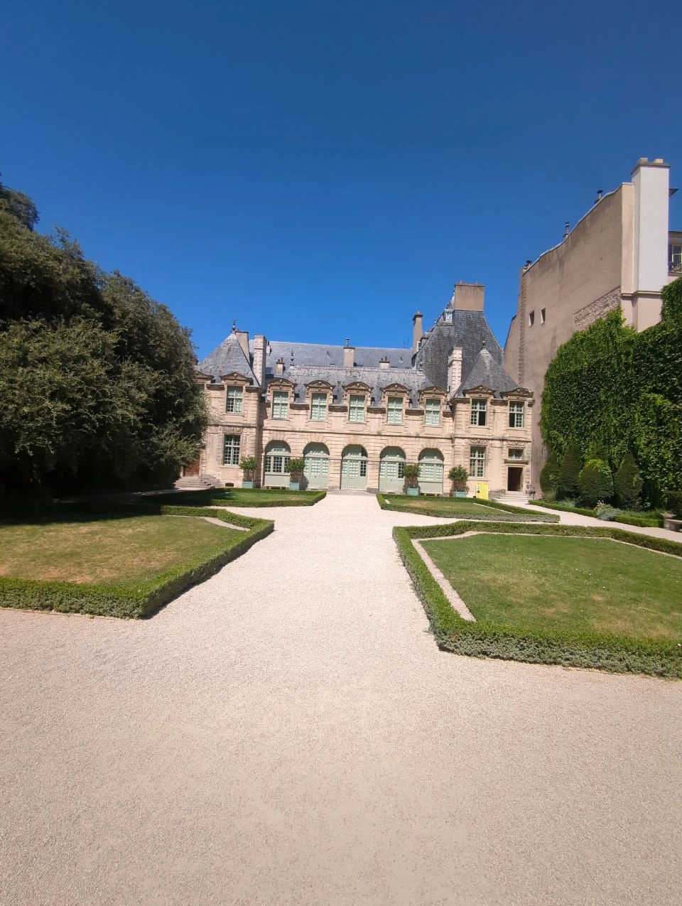 Paris Photoshoot - Hôtel de Sully Courtyard Straight gravel paths and clipped hedges lead toward the pale historic façade of Hôtel de Sully, an access-dependent Paris photoshoot setting.