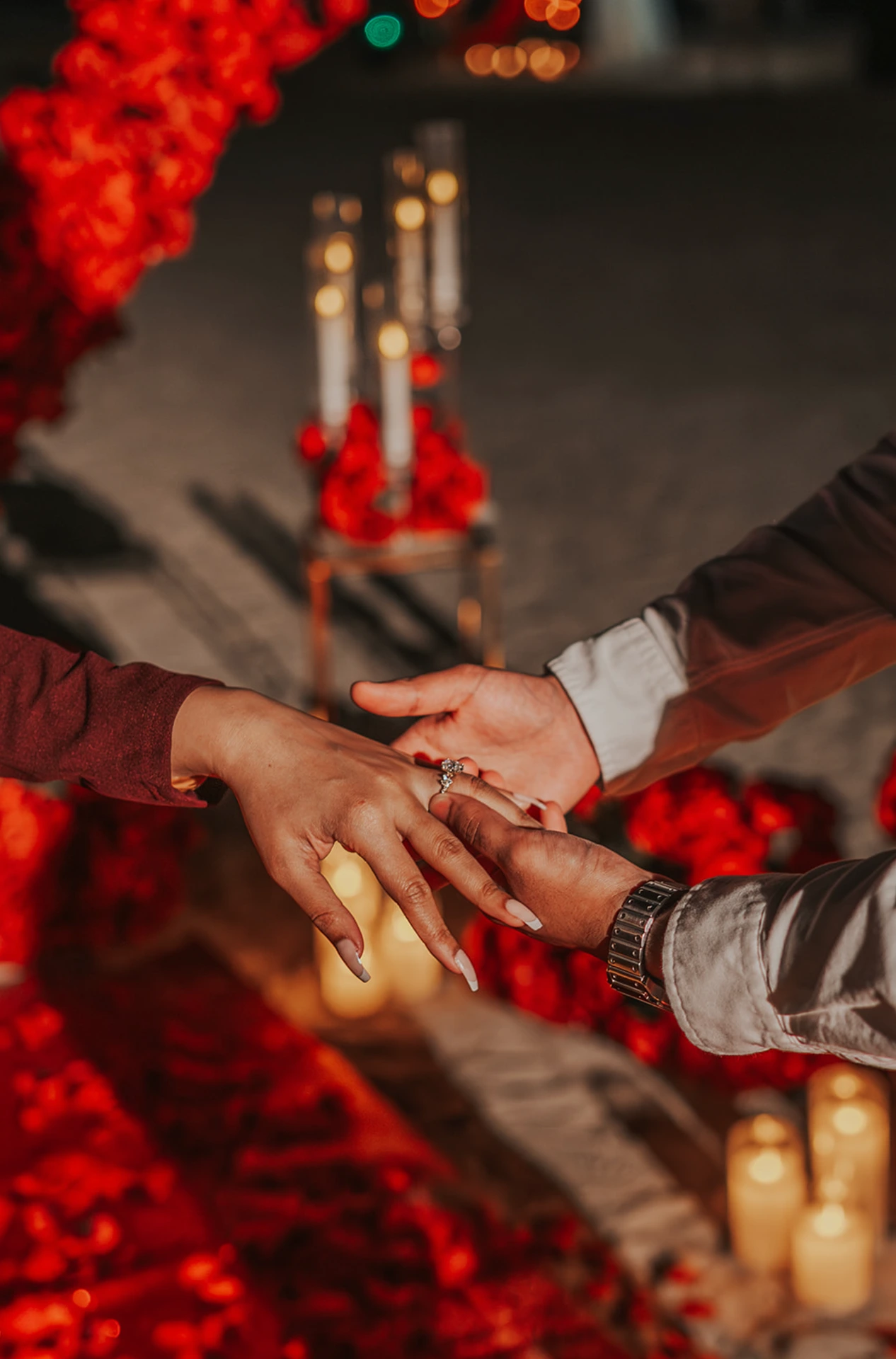 Close-up of a ring being placed on her finger during a Dubai heart proposal setup, with red roses and candlelight softly visible around the hands.