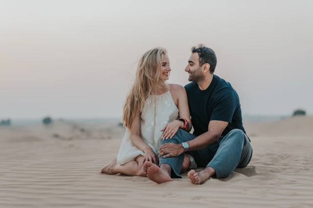 A couple sits together on Dubai desert dunes at sunset during a relaxed outdoor photoshoot.