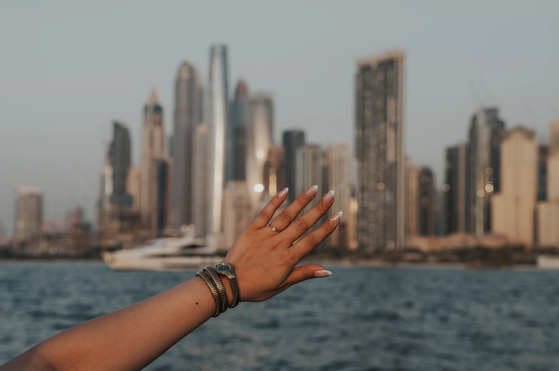 Ring voor de skyline na aanzoek in Dubai Marina Een vrouwenhand toont een solitaire ring voor een jacht en de skyline van Dubai Marina na een huwelijksaanzoek op het water.