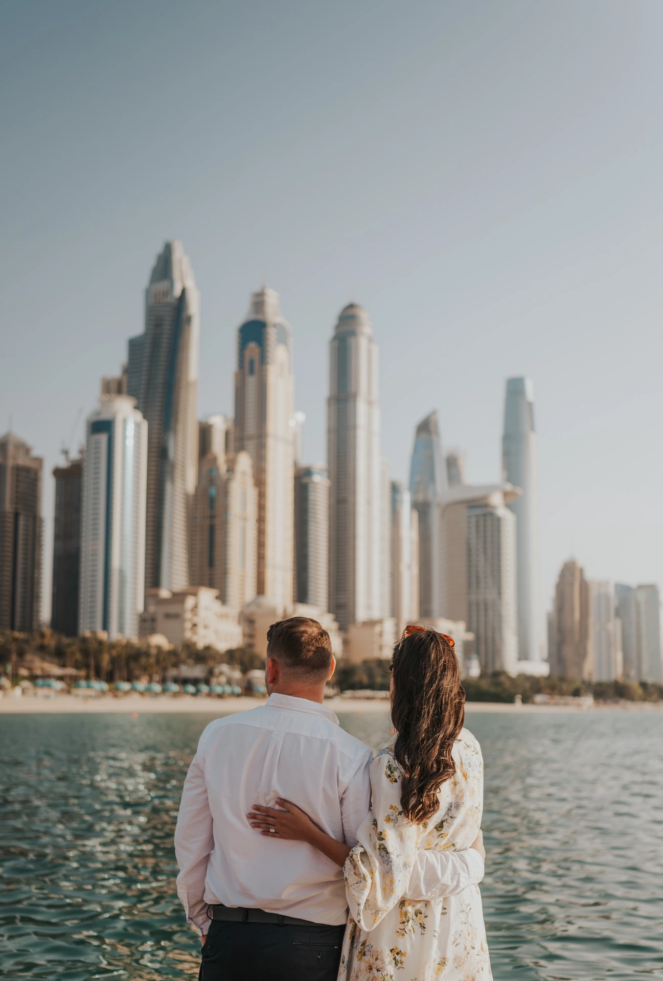 Ring na het aanzoek bij de skyline van Dubai Marina Een koppel omhelst elkaar aan het water terwijl haar ringhand op haar partner rust, met Dubai Marina achter hun huwelijksaanzoekportret.
