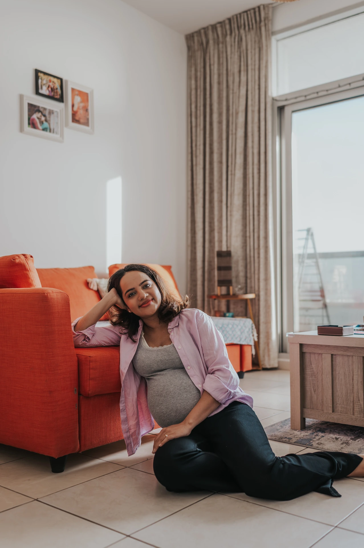 A pregnant woman poses in a Dubai living room during an indoor maternity photoshoot, showing a comfortable at-home style with natural window light.