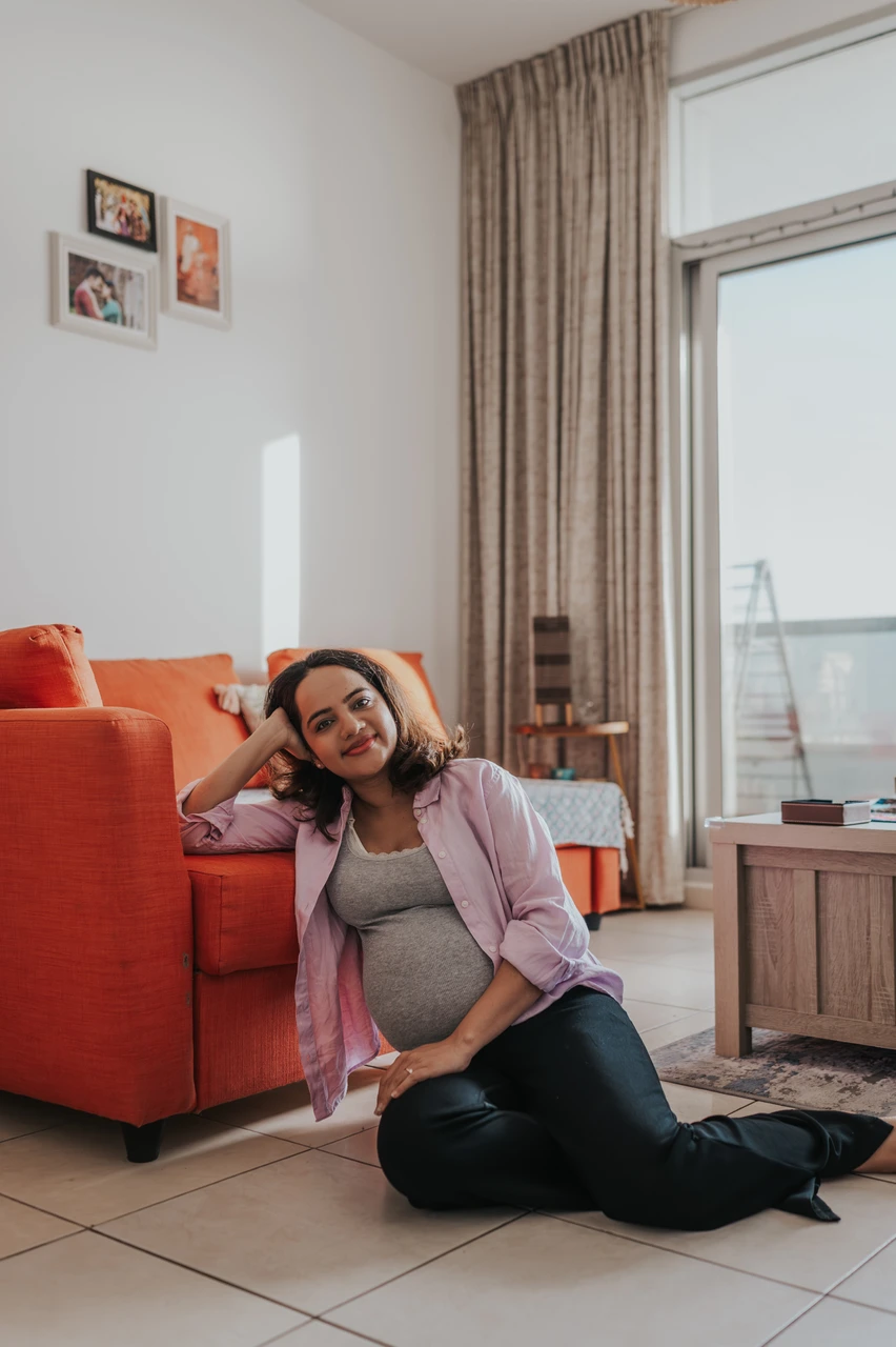 Dubai Maternity Indoor vs Outdoor - living-room solo portrait A pregnant woman poses in a Dubai living room during an indoor maternity photoshoot, showing a comfortable at-home style with natural window light.