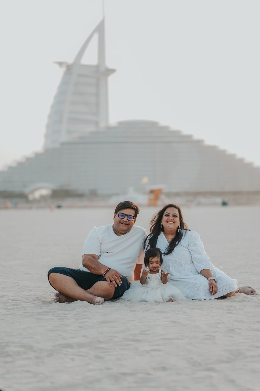 Family beach photoshoot locations Dubai - seated family portrait A family sits together with their toddler on Dubai beach near Jumeirah Beach Hotel during a relaxed family beach photoshoot.
