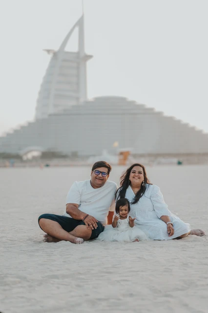 A family sits together with their toddler on Dubai beach near Jumeirah Beach Hotel during a relaxed family beach photoshoot.