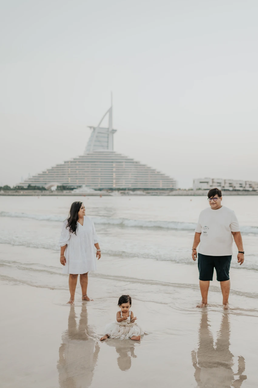 Family beach photoshoot locations Dubai - shoreline walk Jumeirah A couple and toddler stand in shallow water on Dubai beach near Jumeirah Beach Hotel during a relaxed family photoshoot.