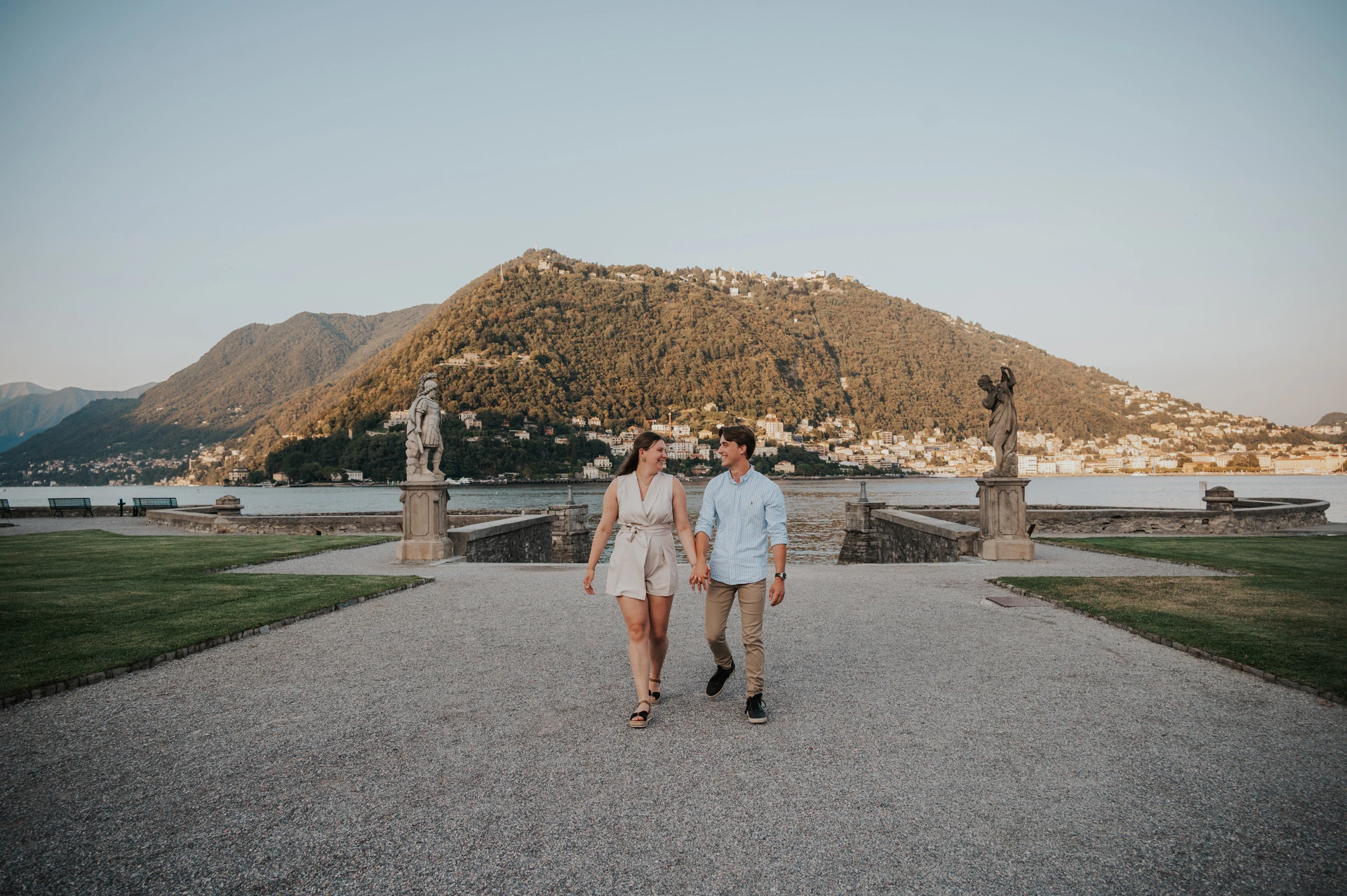 Couple walking along the wide path between stone pillars during their Lake Como couple photoshoot at Villa Olmo.