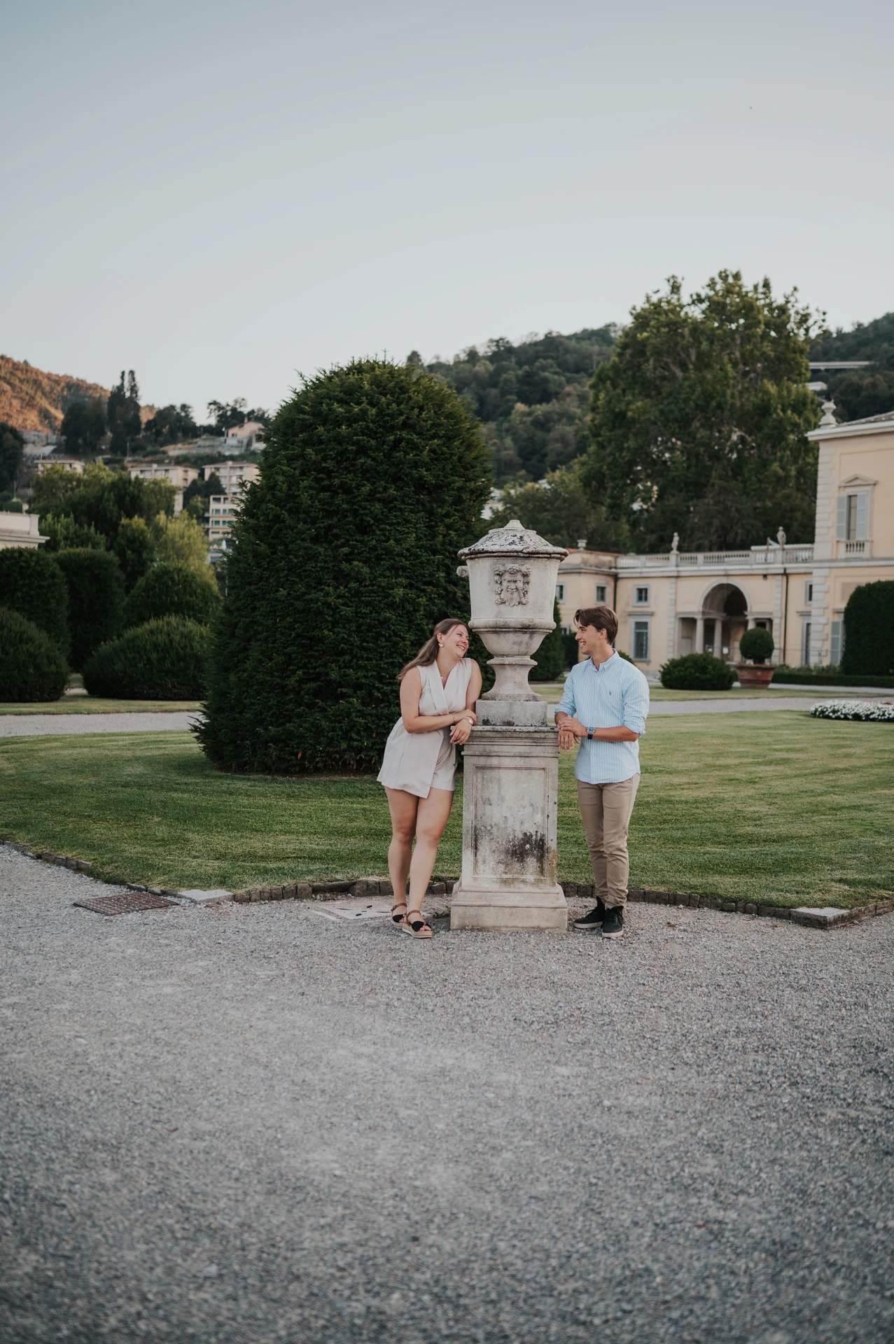 Couple standing on either side of a stone pillar among clipped trees during their Lake Como couple photoshoot in Villa Olmo’s gardens.