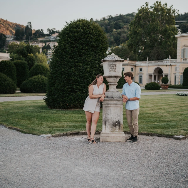 Lake Como couple photoshoot with Villa Olmo’s garden details Wide garden portrait of the couple beside a carved stone pillar during their Lake Como couple photoshoot at Villa Olmo.