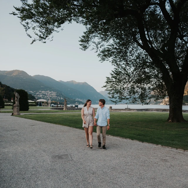 Lake Como couple photoshoot beneath the garden trees Couple walking along a broad garden path beneath a leafy tree during their Lake Como couple photoshoot at Villa Olmo.