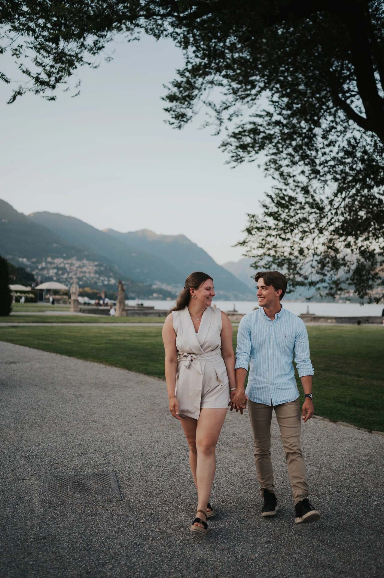 Couple holding hands beneath a tree by the lake during their Lake Como couple photoshoot in Villa Olmo’s gardens.