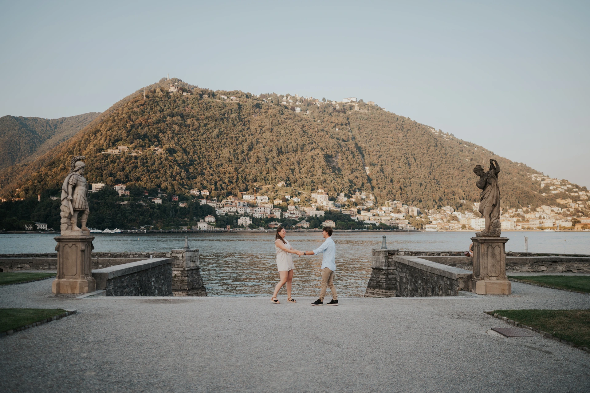 Couple turning together on a broad path between stone pillars during their Lake Como couple photoshoot in Villa Olmo’s gardens.