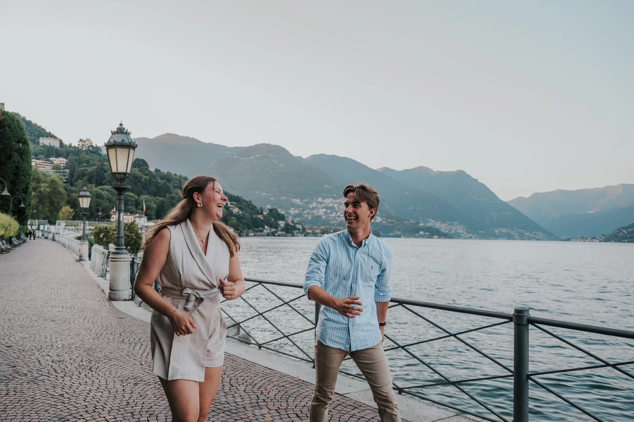 Lake Como couple photoshoot walking along the promenade Couple holding hands while walking along the waterfront railing during their Lake Como couple photoshoot in Como.