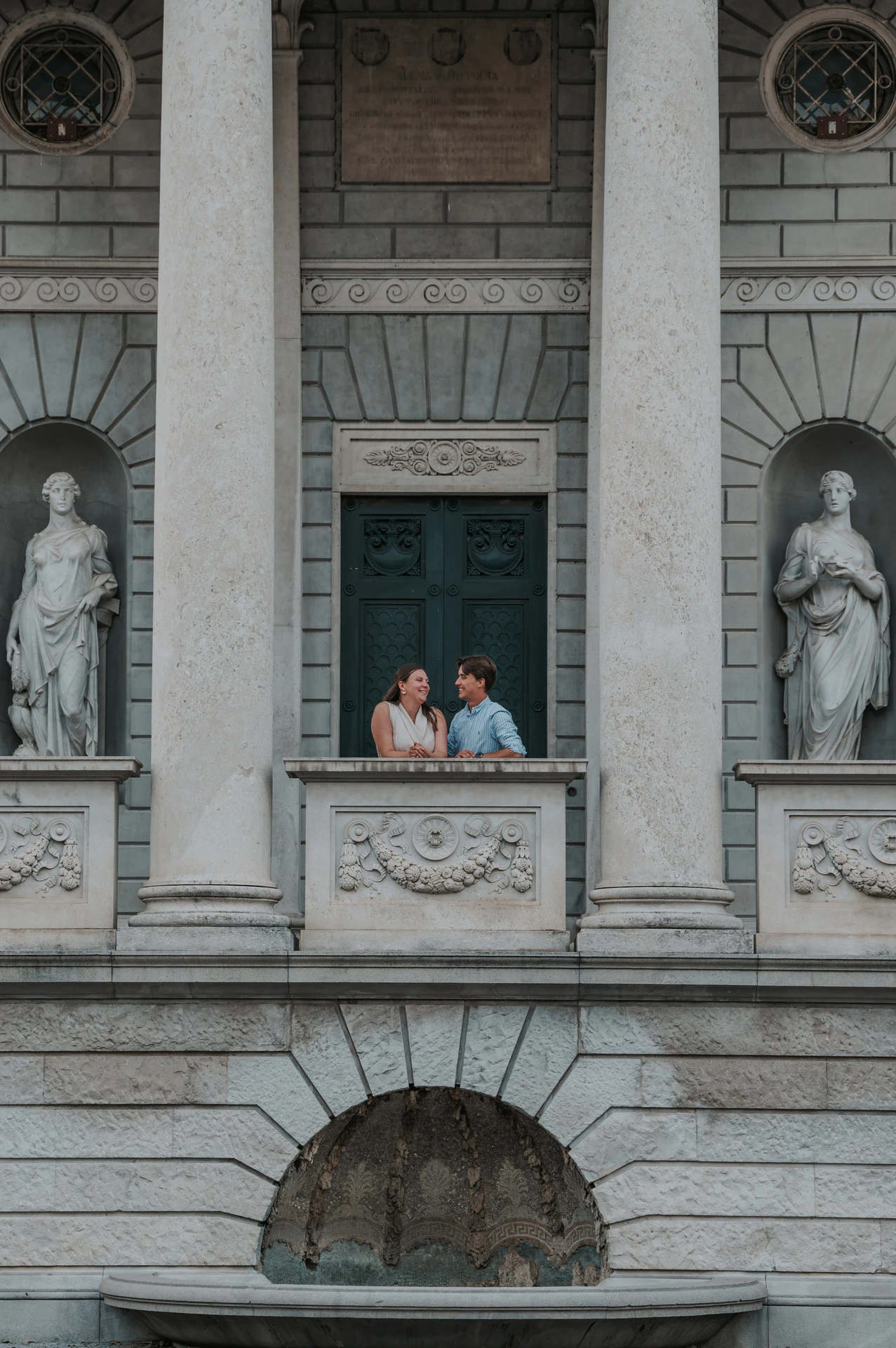 Couple looking out from Tempio Voltiano’s carved stone balcony between statues during their Lake Como couple photoshoot.