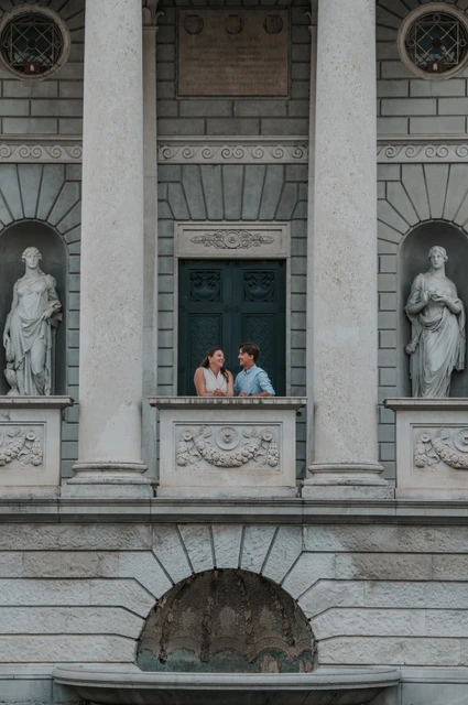 Lake Como couple photoshoot on Tempio Voltiano’s stone balcony Couple looking out from Tempio Voltiano’s carved stone balcony between statues during their Lake Como couple photoshoot.