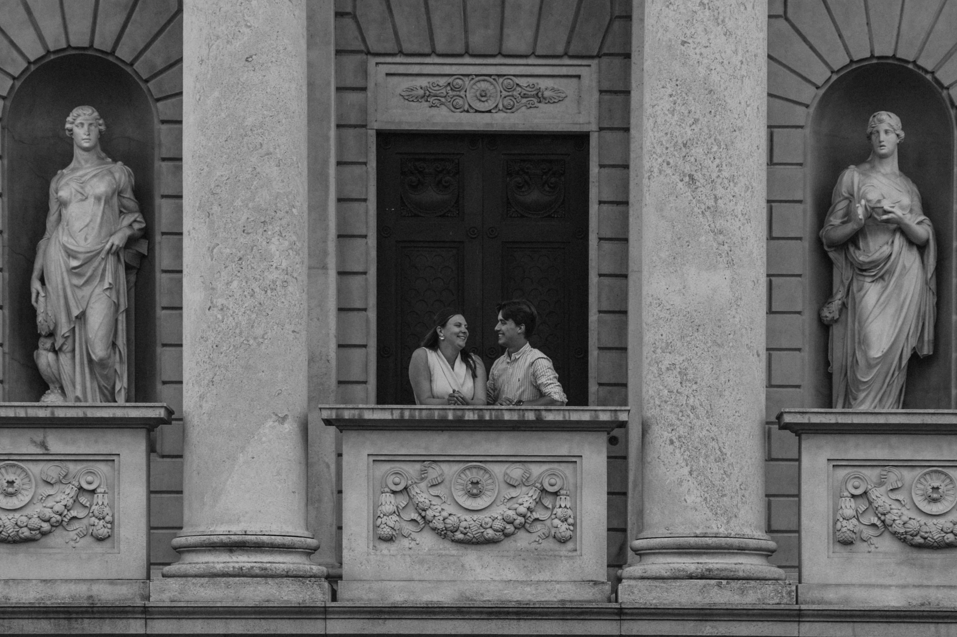 Black-and-white portrait of the couple on Tempio Voltiano’s stone balcony between statues during their Lake Como couple photoshoot.