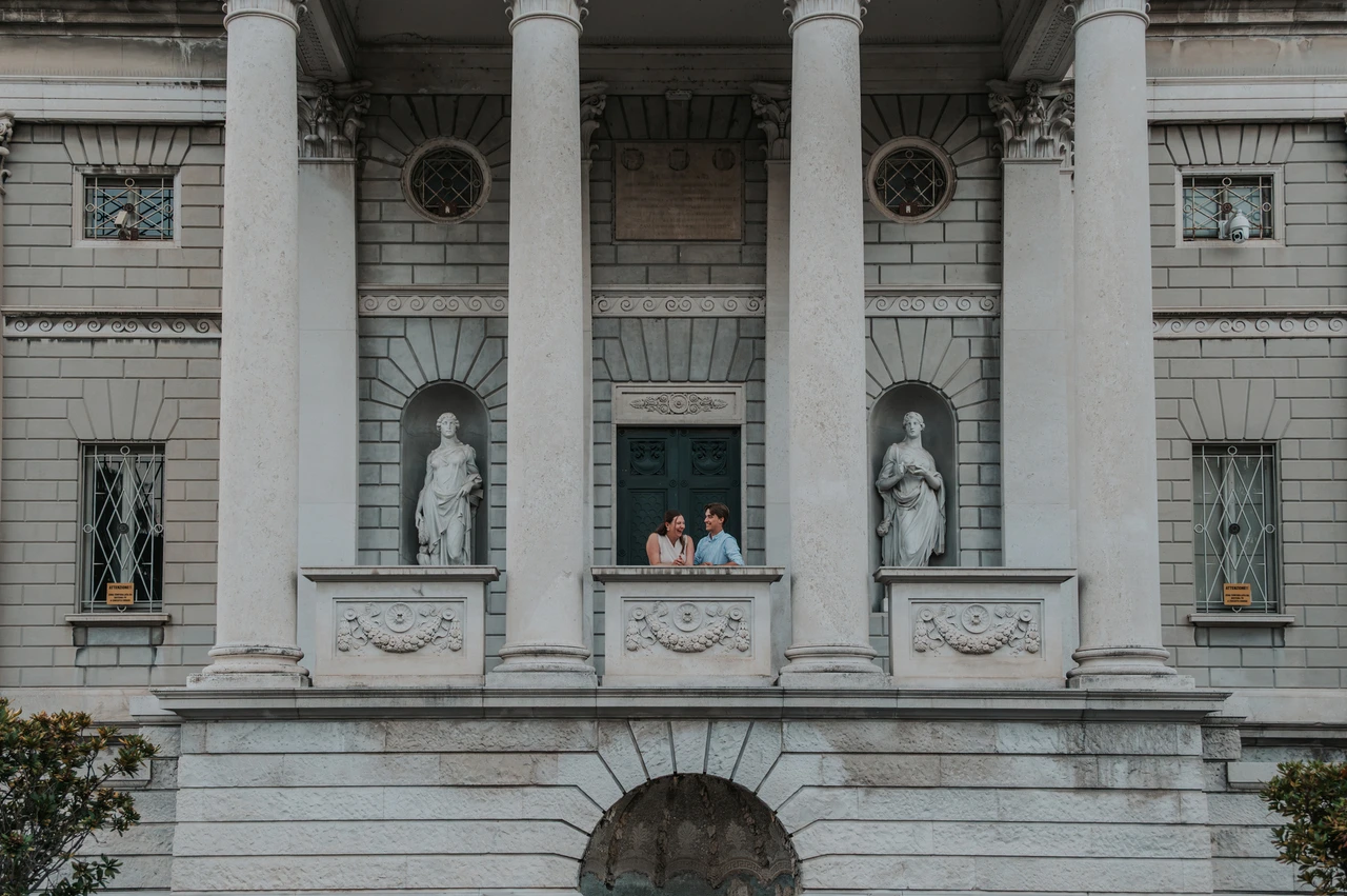 Lake Como couple photoshoot framed by Tempio Voltiano’s columns Wide view of Tempio Voltiano’s columns and carved stone balcony with the couple during their Lake Como couple photoshoot.