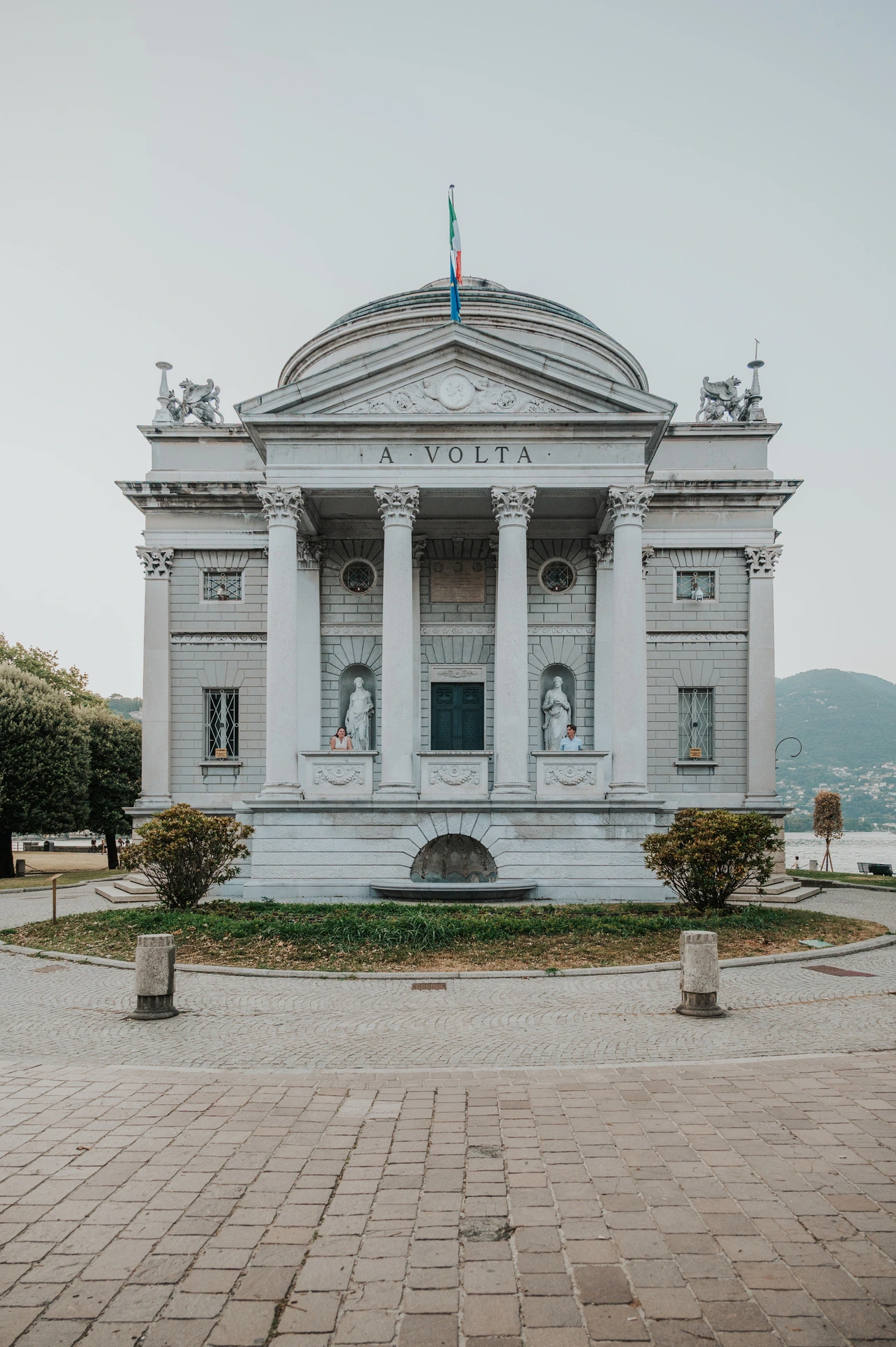 Lake Como couple photoshoot at Tempio Voltiano Couple standing by the columns of Tempio Voltiano during their Lake Como couple photoshoot, with the full neoclassical facade in view.
