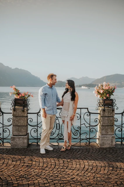 Lake Como engagement photoshoot between Menaggio’s flower-filled pillars The couple stand between flower-filled stone pillars and ornate iron railings during their Lake Como engagement photoshoot in Menaggio.