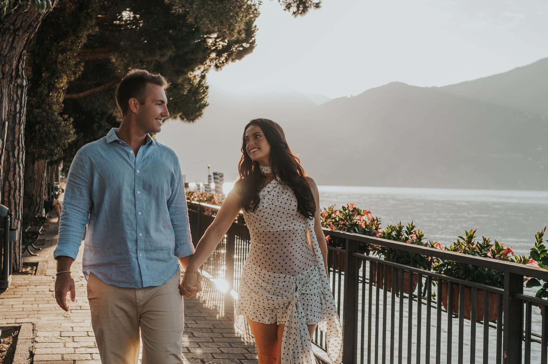 The couple smile at each other while walking beside Menaggio’s lakeside railing during their Lake Como photoshoot.