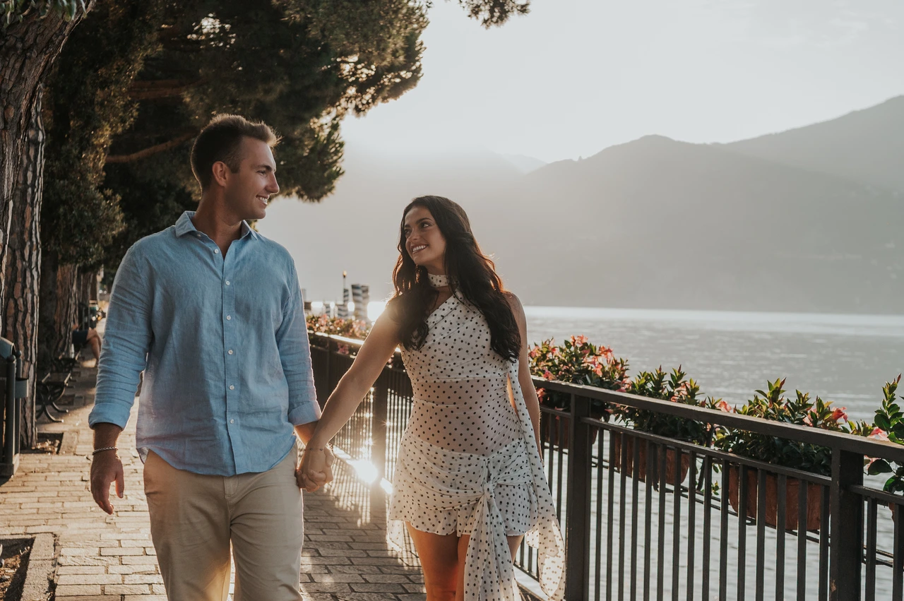 Lake Como photoshoot walking together beside the Menaggio water The couple smile at each other while walking beside Menaggio’s lakeside railing during their Lake Como photoshoot.