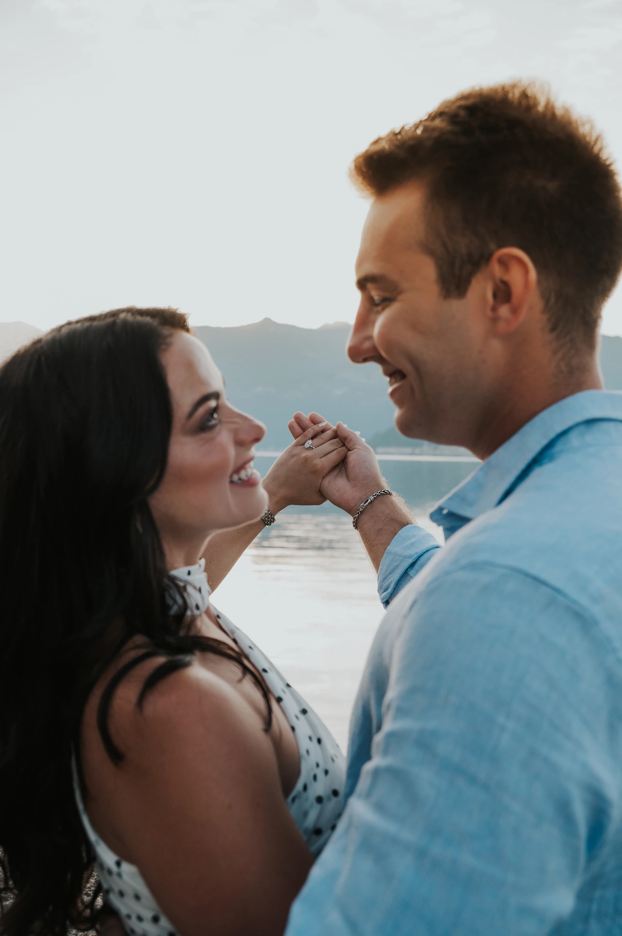 The couple look at each other with their joined hands raised beside their faces during their Lake Como engagement photoshoot by the water.