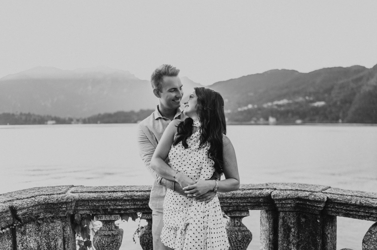 Black-and-white Lake Como photoshoot at the lakeside balustrade Black-and-white portrait of the couple embracing by the stone balustrade, with the lake behind them during their Lake Como photoshoot.
