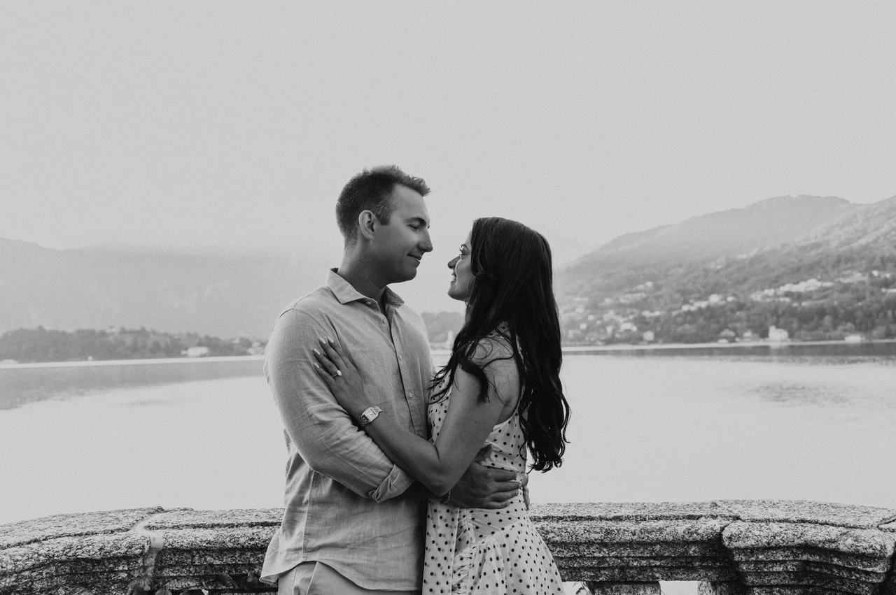 Black-and-white Lake Como engagement photoshoot on the lake terrace Black-and-white photograph of the couple smiling face to face beside the stone terrace railing during their Lake Como engagement photoshoot.