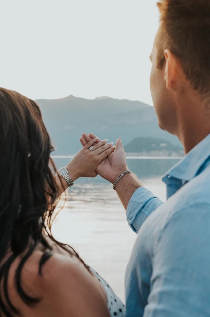 Lake Como engagement photoshoot with the ring seen over their shoulders Seen over the couple’s shoulders, their joined hands and her ring are held against the lake view during their Lake Como photoshoot.