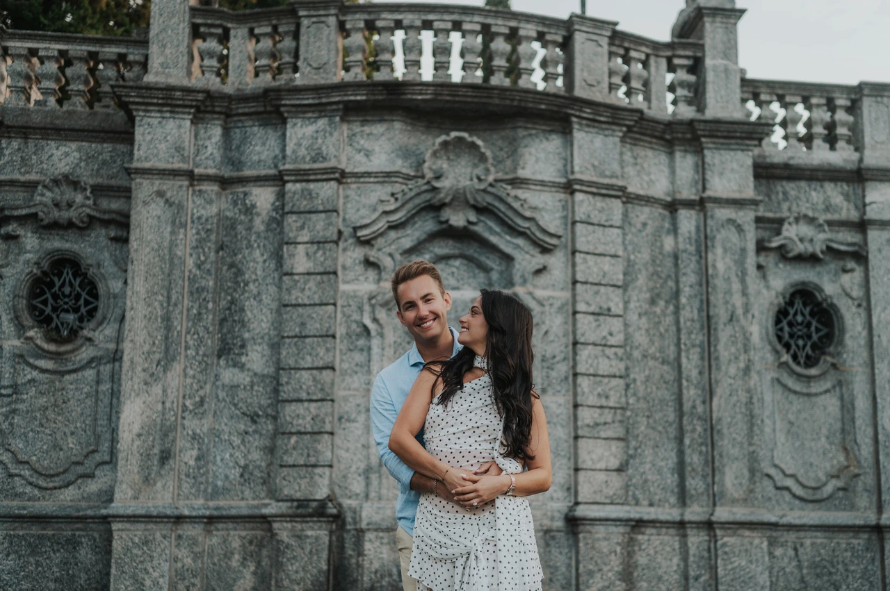Lake Como photoshoot portrait beside the decorative stone wall The couple smile together in front of decorative stone panels and a balustrade during their Lake Como photoshoot at Parco Civico Teresio Olivelli.