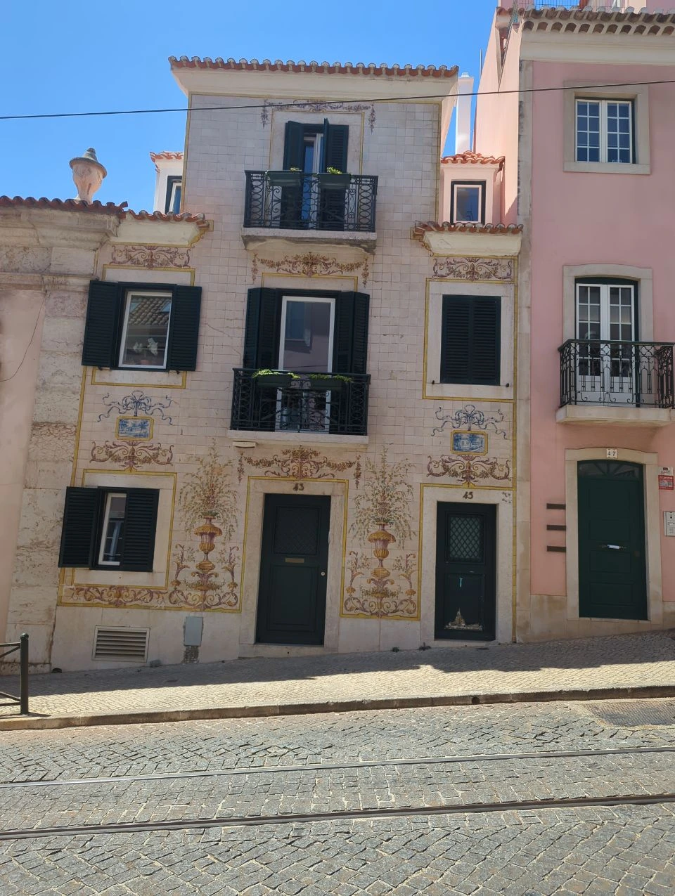Floral tiles frame the doors and windows of numbers 43 and 45 along a sunlit Lisbon photoshoot route through Lapa.