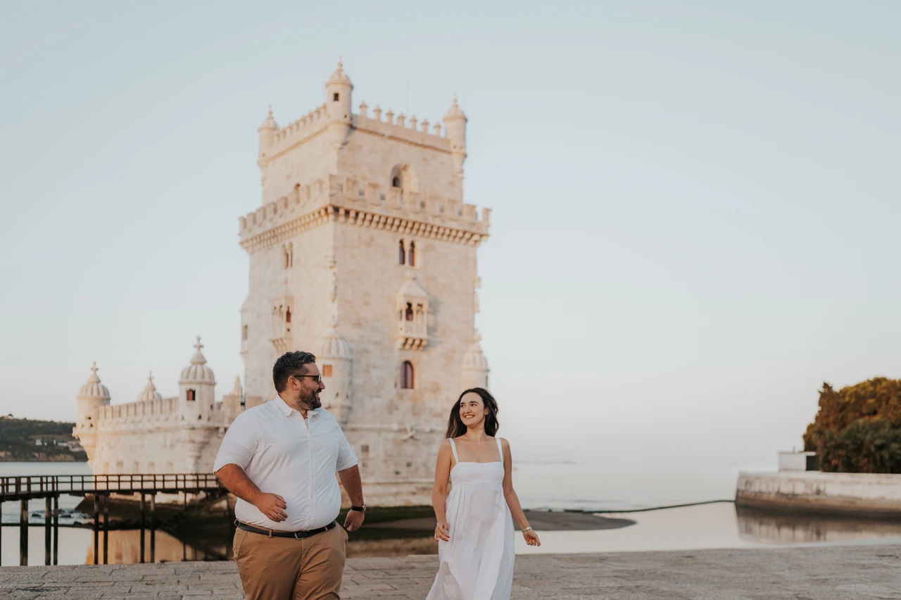 Smiling at each other beside the tower | Lisbon anniversary photoshoot The couple standing apart and smiling at each other beside Belém Tower during their anniversary photoshoot in Lisbon.