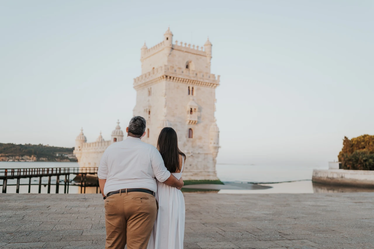 An arm around her with the tower ahead | Lisbon anniversary photoshoot A landscape portrait of the couple from behind with an arm around her and Belém Tower ahead during their anniversary photoshoot in Lisbon.