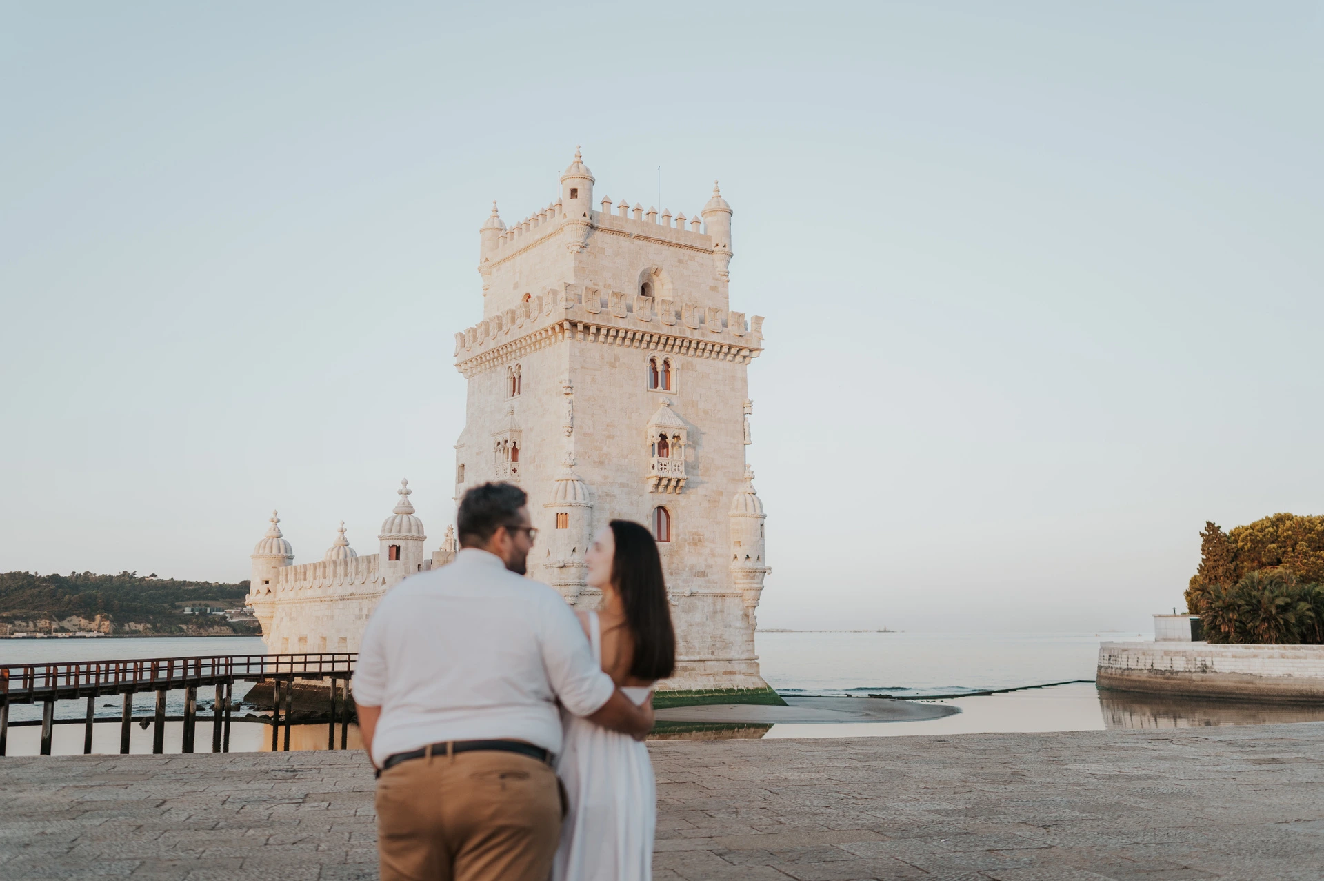 The couple turning towards each other while standing with their backs to the camera by Belém Tower during their anniversary photoshoot in Lisbon.