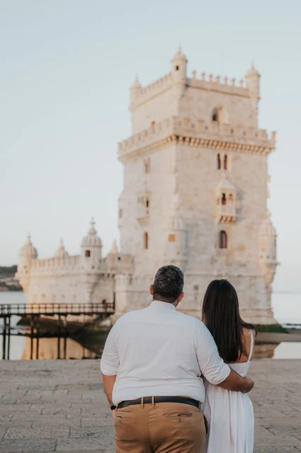 Looking towards the tower together | Lisbon anniversary photoshoot The couple seen from behind with his arm around her as they look towards Belém Tower during their anniversary photoshoot in Lisbon.