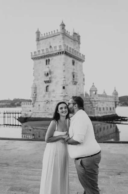 A cheek kiss in black and white | Lisbon anniversary photoshoot A black-and-white portrait of the man kissing his partner on the cheek by Belém Tower during their anniversary photoshoot in Lisbon.