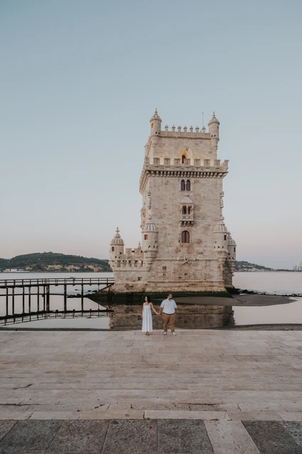 A distant portrait beside the tower | Lisbon anniversary photoshoot The couple standing together at a distance on the stone paving beside Belém Tower during their anniversary photoshoot in Lisbon.