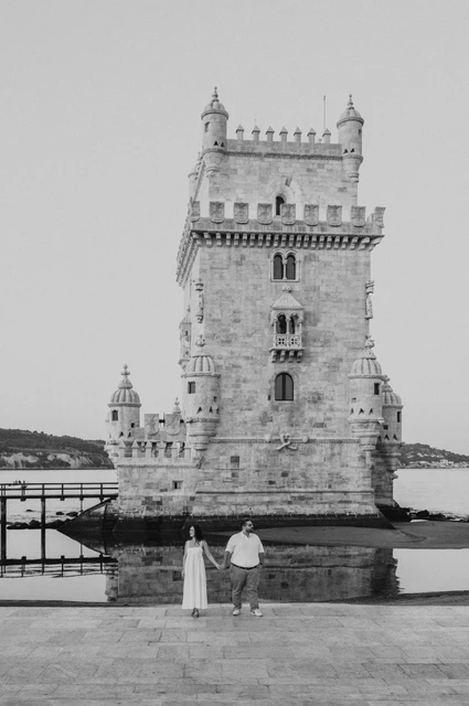 The tower and couple in black and white | Lisbon anniversary photoshoot A black-and-white view of Belém Tower with the couple standing hand in hand below it during their anniversary photoshoot in Lisbon.