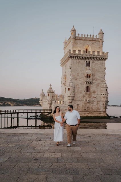 Joined hands beneath the tower | Lisbon anniversary photoshoot The couple holding hands on the waterfront with the full Belém Tower in view during their anniversary photoshoot in Lisbon.