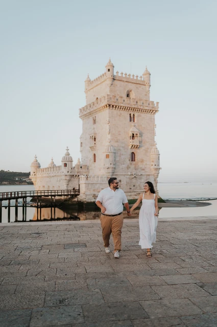 Walking together past Belém Tower | Lisbon anniversary photoshoot A full-length portrait of the couple walking together beside Belém Tower during their anniversary photoshoot in Lisbon.